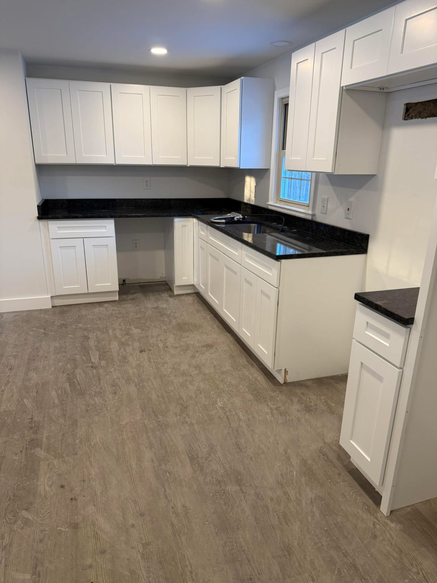 Remodeled kitchen with white shaker cabinets and dark granite counters