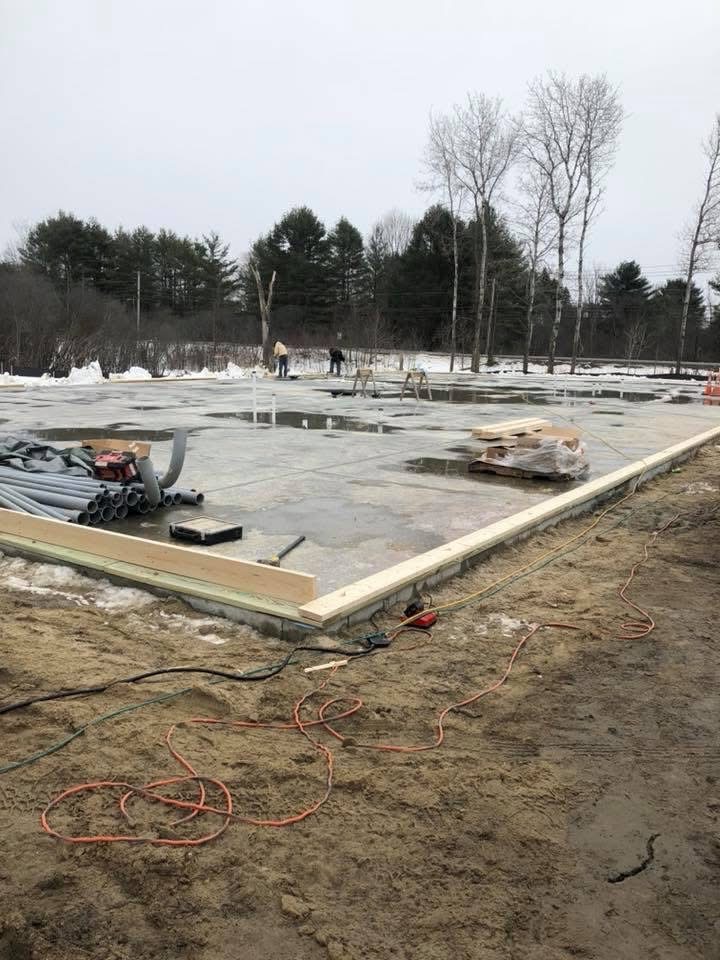 Concrete slab poured with sill plates staged for framing on a winter jobsite