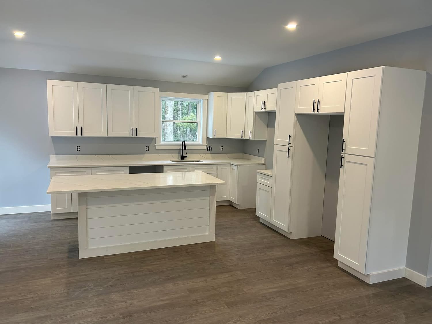 New kitchen with white cabinetry, quartz island, and hardwood-style flooring