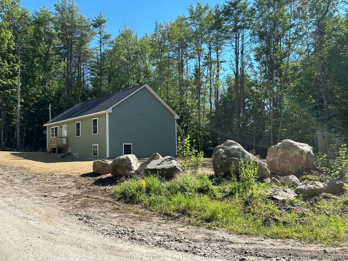 Side view of a newly built green ranch home on a wooded Maine lot
