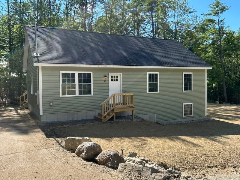 Completed green ranch home with white trim and wood entry steps