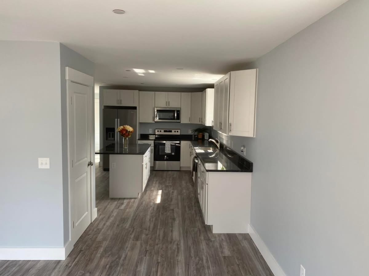 New kitchen viewed from the hallway with white cabinets and gray plank flooring