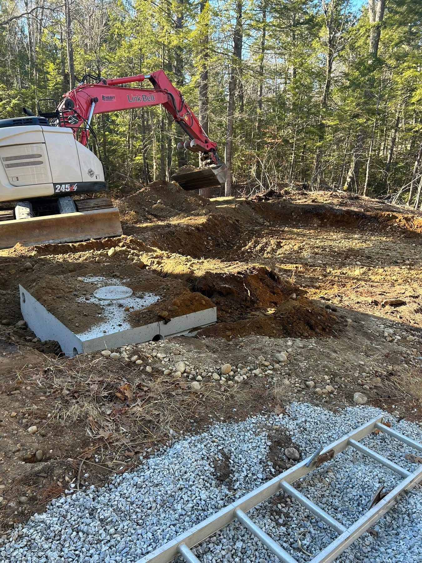Excavator setting a concrete septic tank on a wooded Maine lot