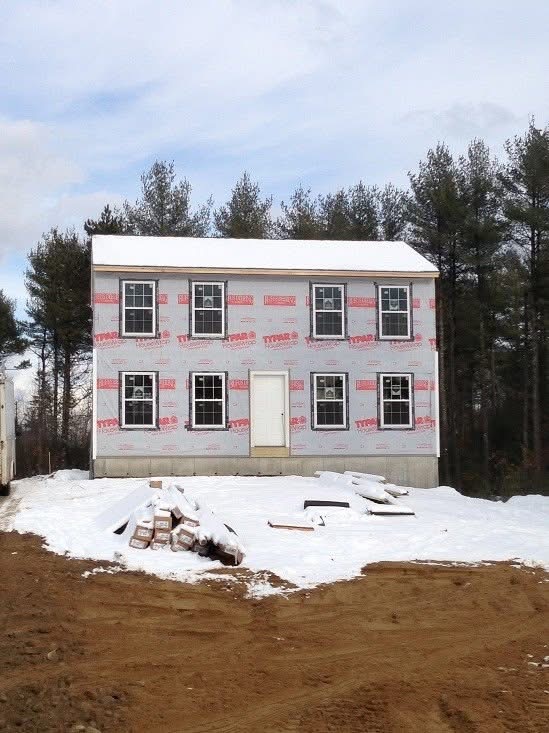 Two-story colonial wrapped in house wrap with windows set during winter